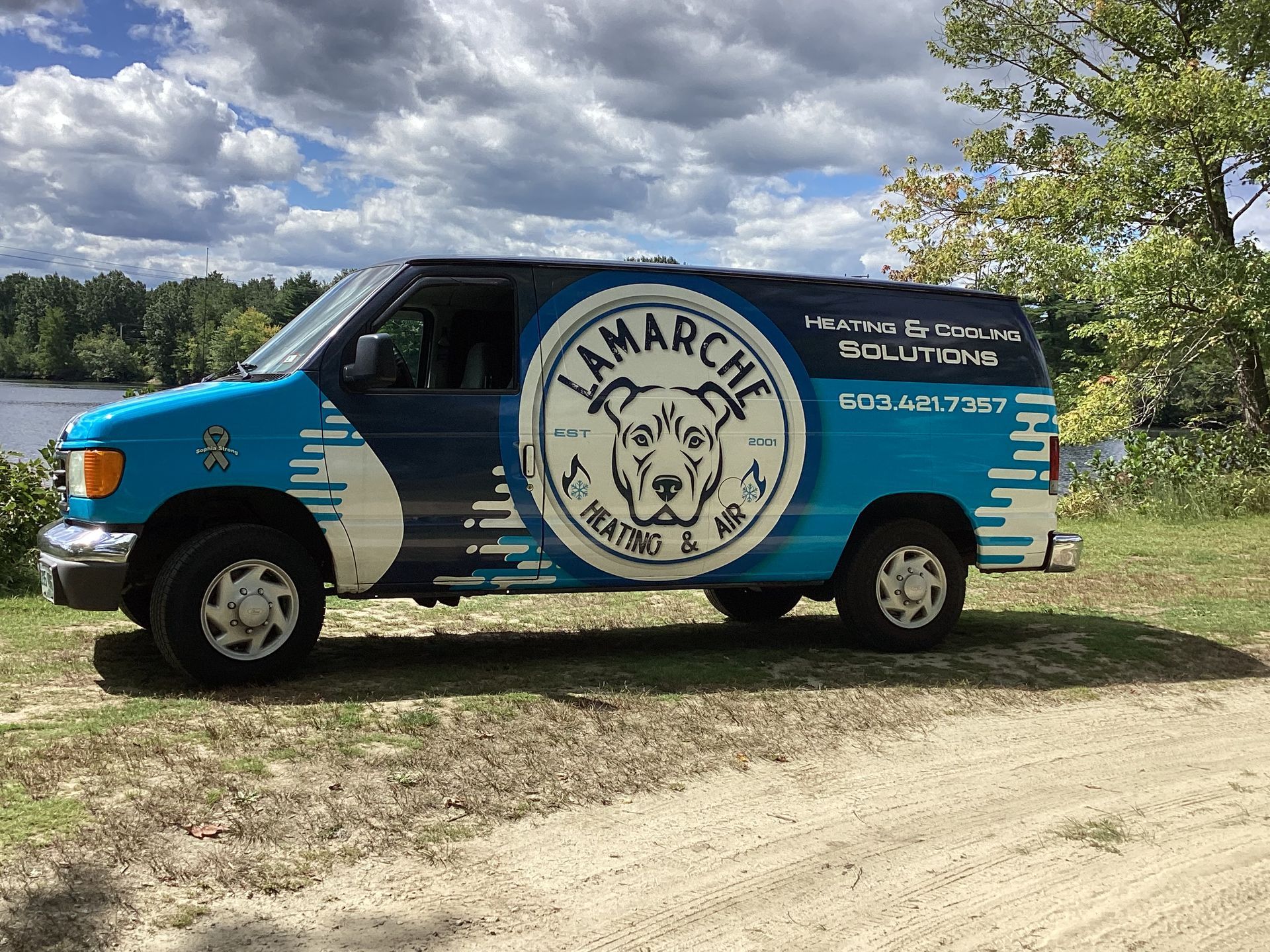 A blue and navy van with the Lamarche Heating & AC Solutions logo parked on a dirt road near a body of water and trees.