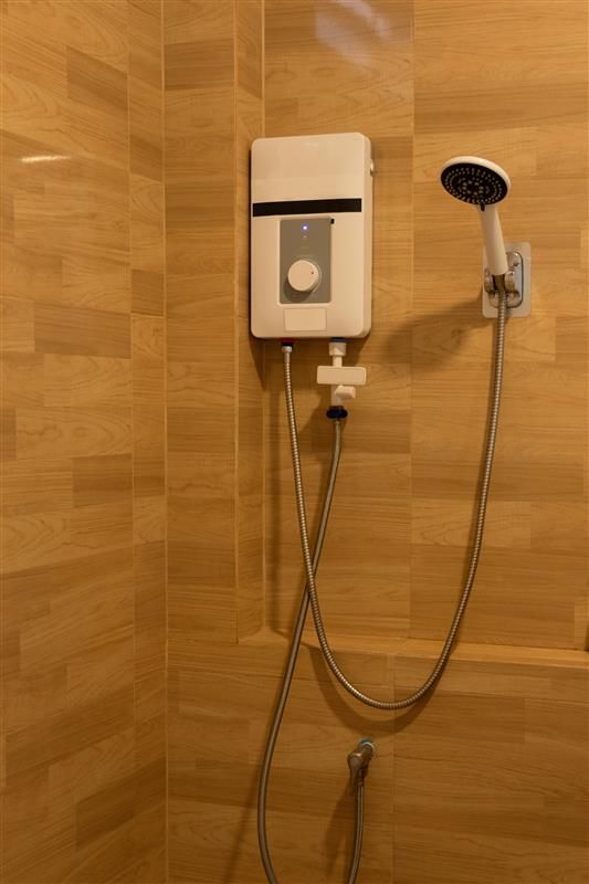 White electric shower unit and handheld shower head on a tiled wall.