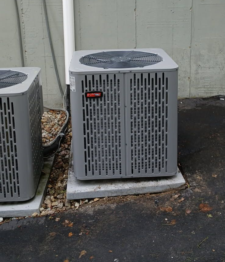 Two gray HVAC outdoor condenser units sit on concrete pads against a gray exterior wall.