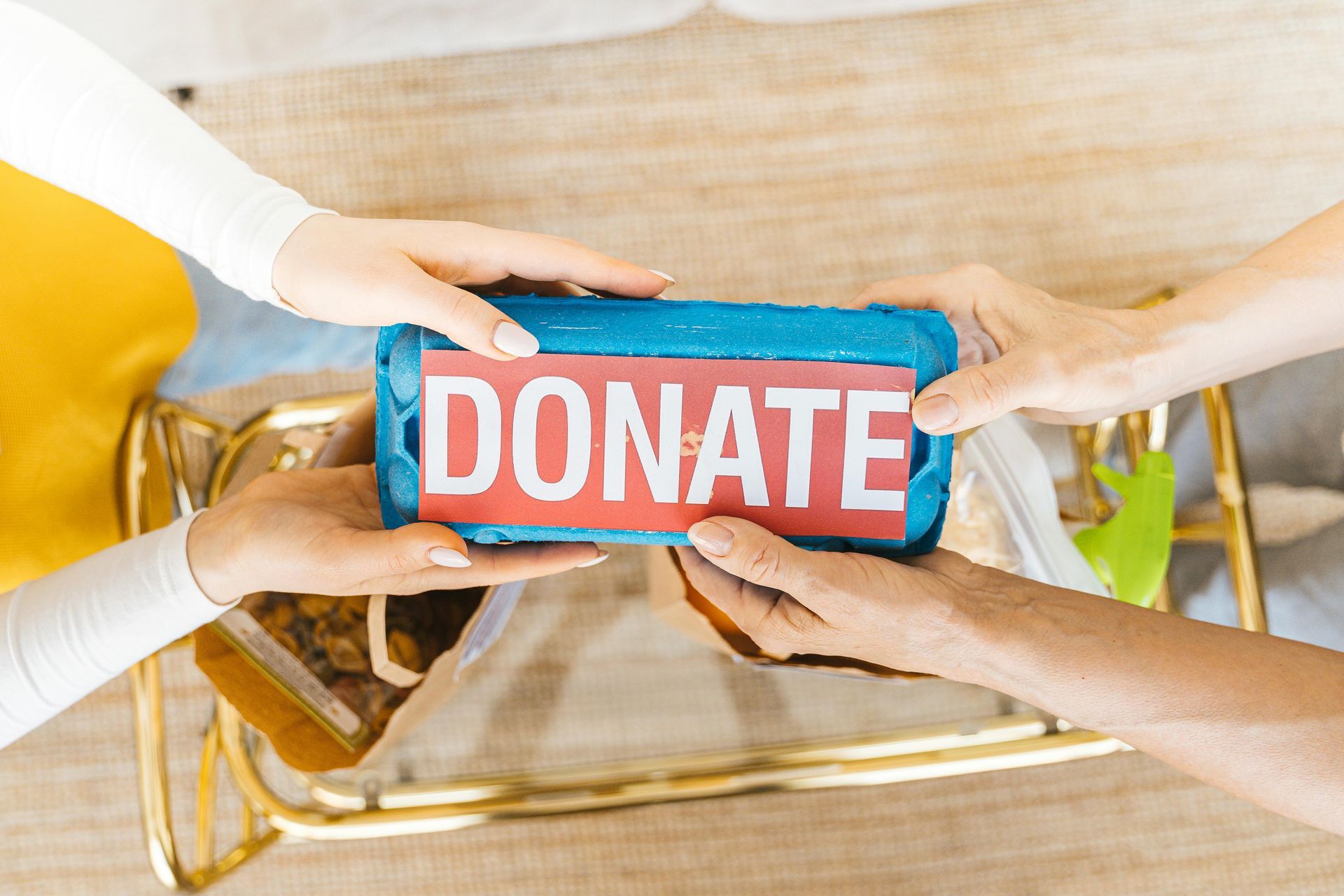 Hands holding a blue box with pink letters spelling “DONATE” over a table