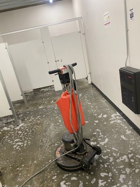 A person using a floor buffer in a commercial kitchen to clean a gray speckled floor.