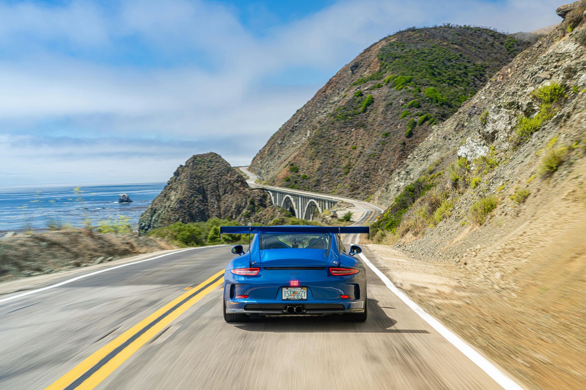 A blue sports car is driving down a mountain road.