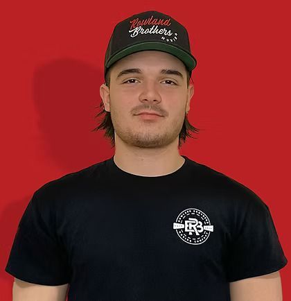 Man in black cap and t-shirt with logo, against red backdrop.
