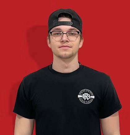 Man wearing glasses and a backwards black cap; black shirt with a white logo; red background.