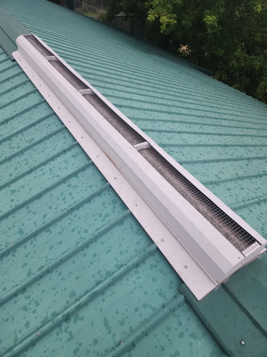 Long white roof vent on a green corrugated metal roof