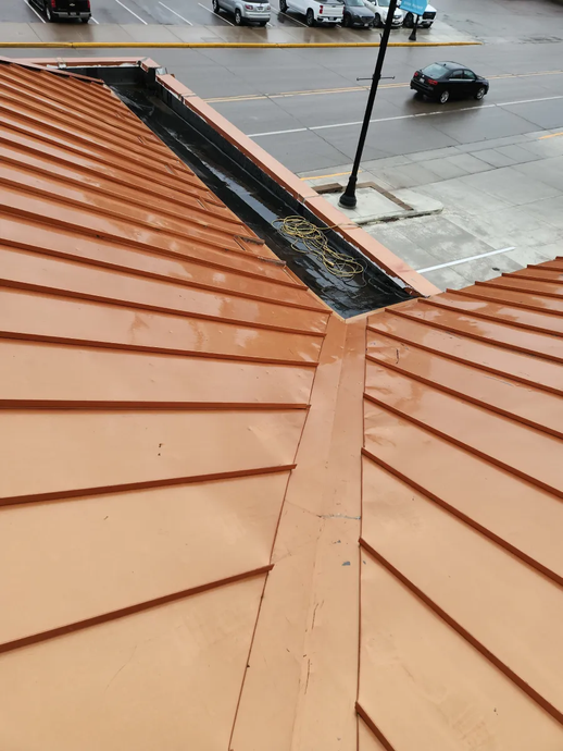 Rooftop with orange metal seams overlooking a wet street and parked cars below