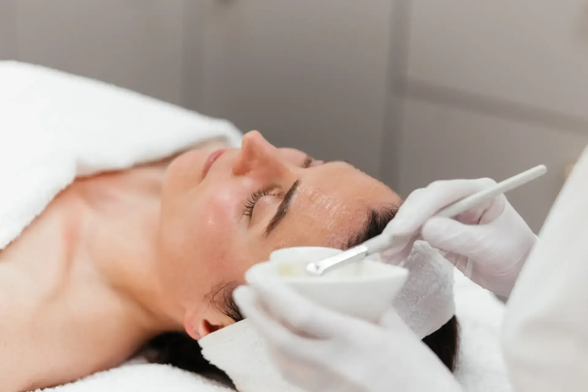 Person receiving a facial treatment with a handheld device while lying on a treatment bed
