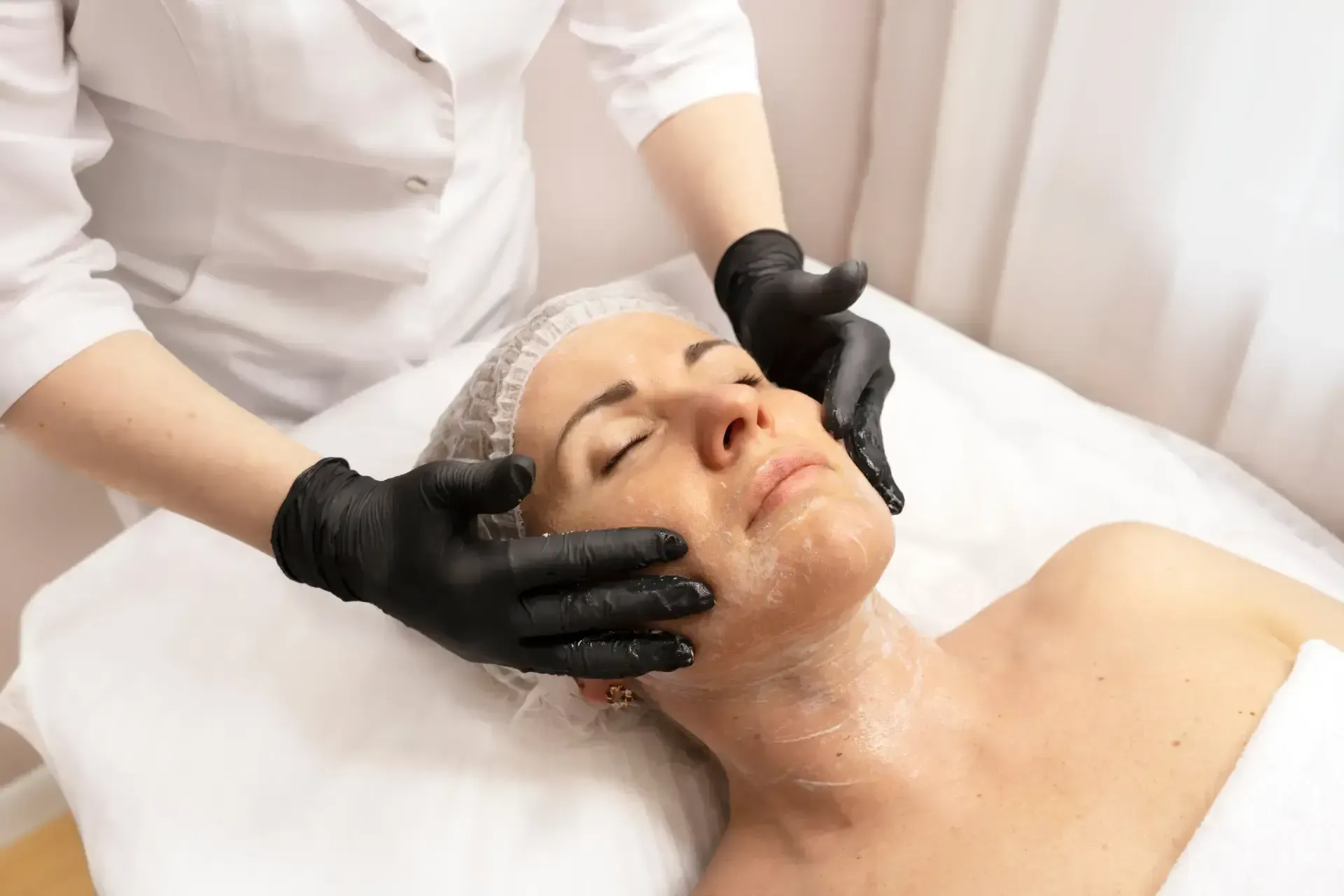 Facial treatment massage with gloved hands on a reclining client in a spa setting