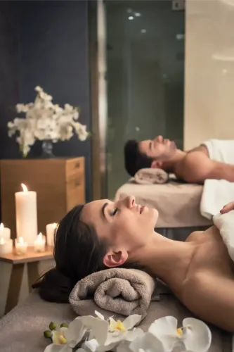 Two people relaxing during a spa treatment with candles, flowers, and towels in a dim room