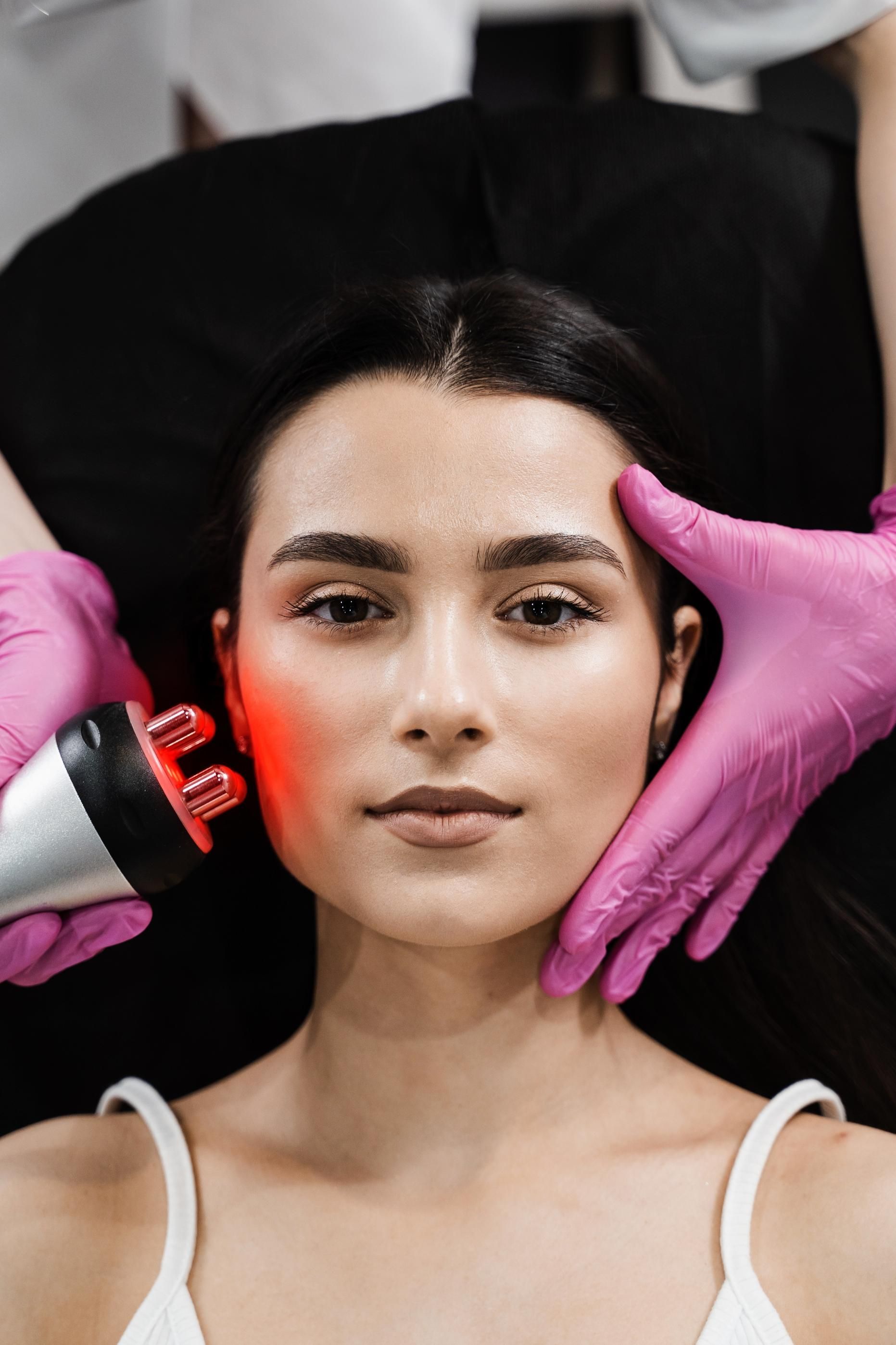 Woman lying on a salon chair while gloved hands shape her face for a beauty treatment.