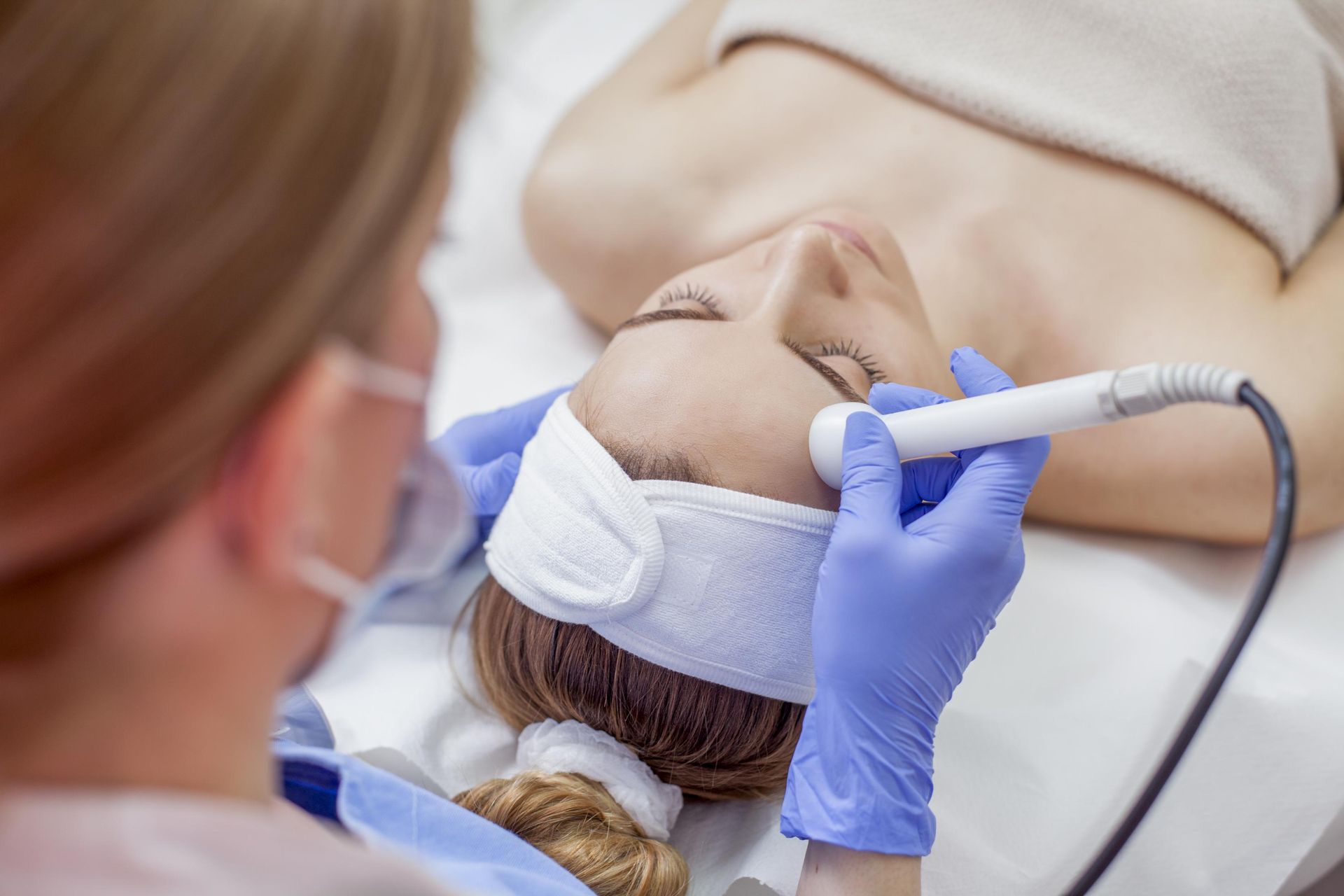 Healthcare worker performing a facial treatment with a handheld device on a reclined patient