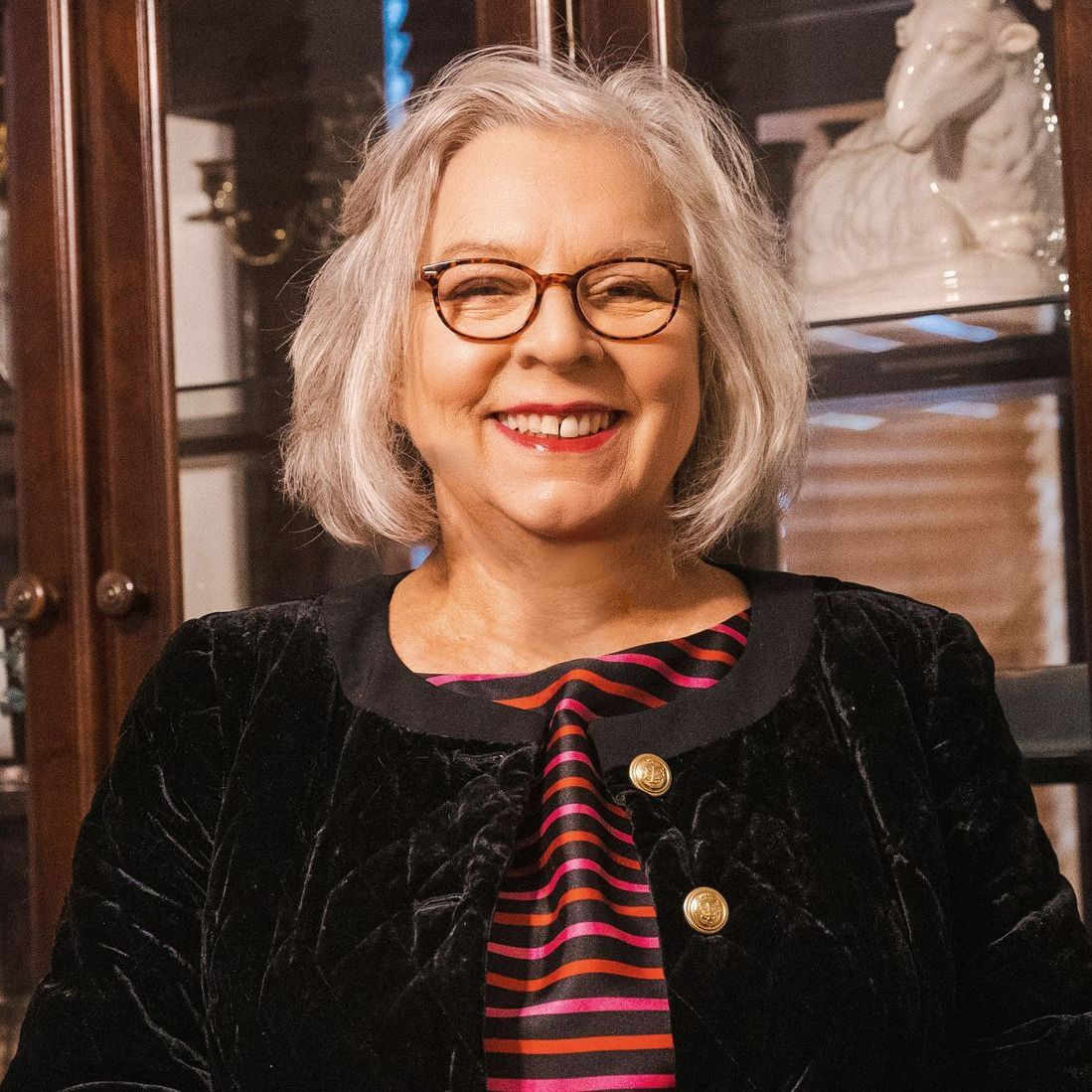 A woman wearing glasses and a black jacket is smiling for the camera.