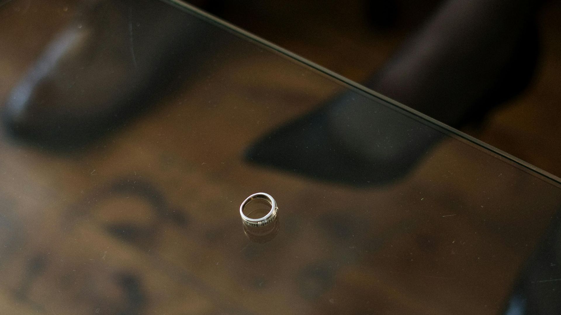 A wedding ring is sitting on a glass table.