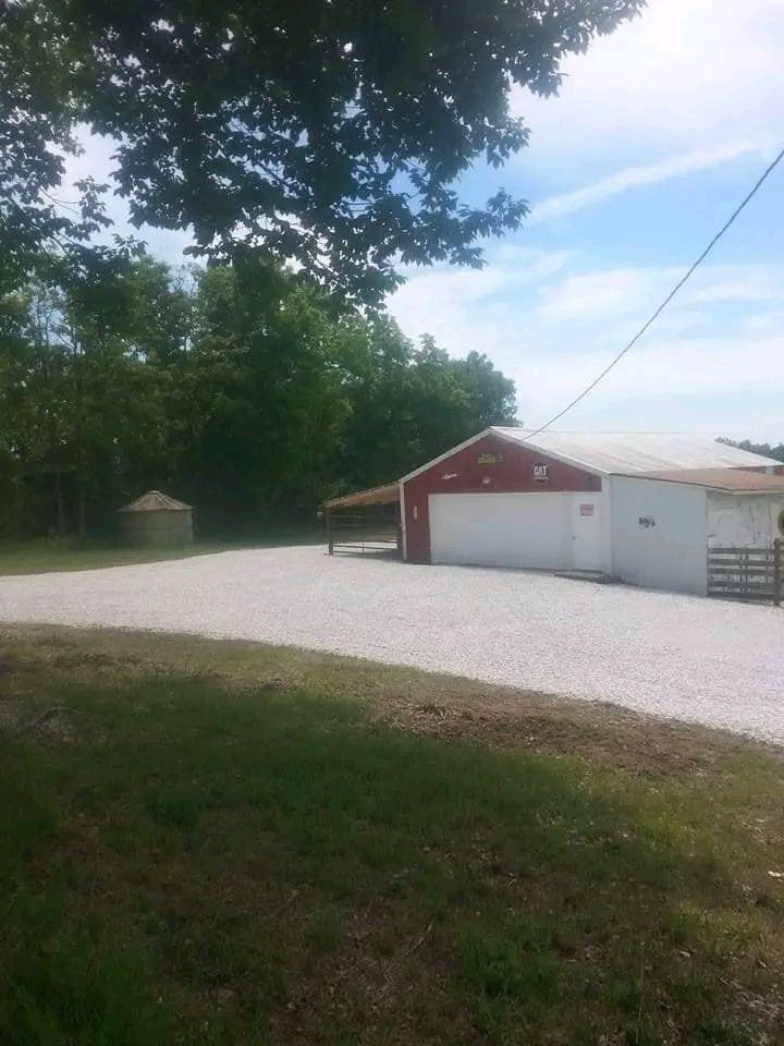 Gravel driveway beside a red garage and white outbuilding under trees and a blue sky