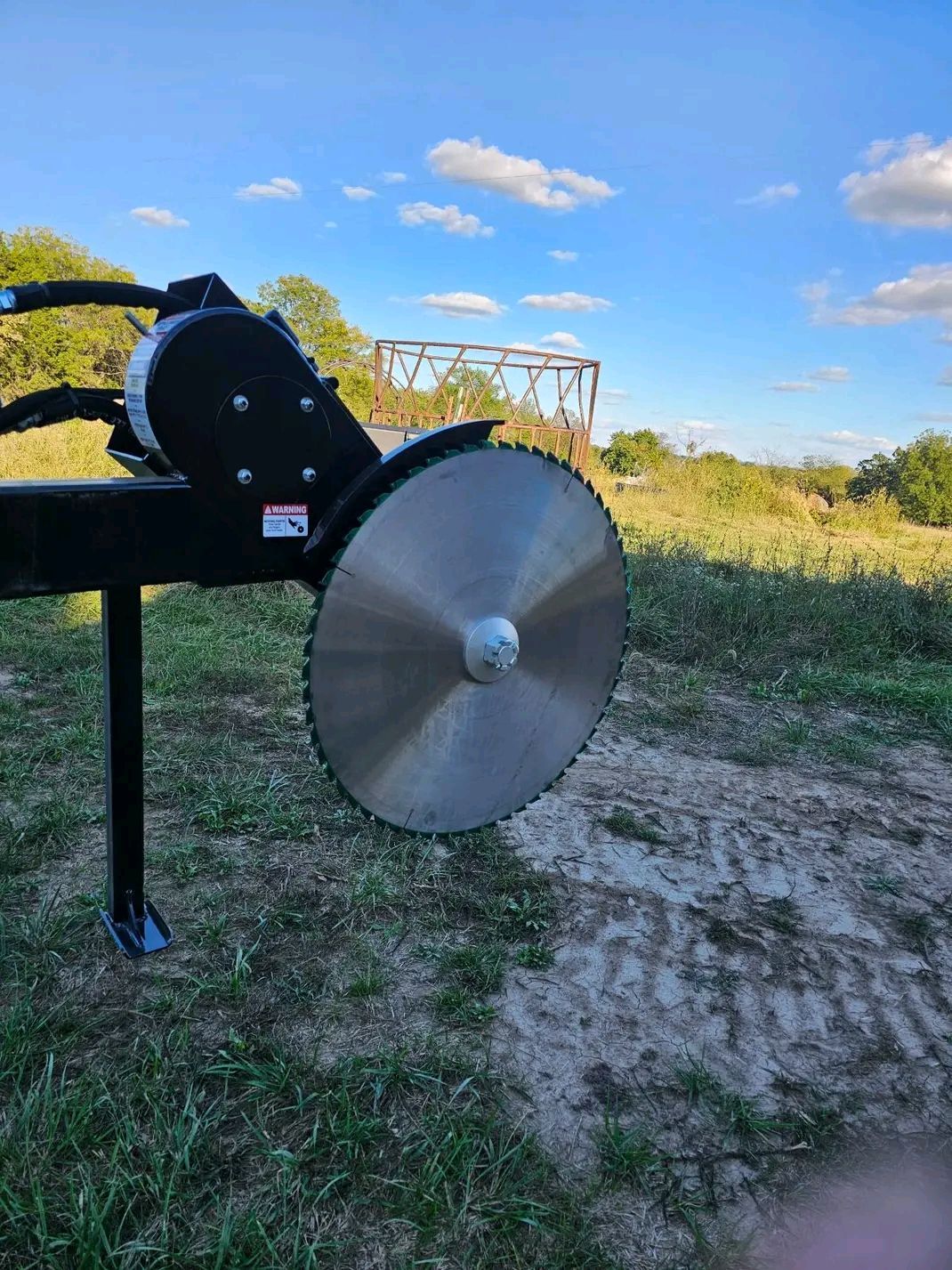 Large metal disk on a black stand in a grassy field under a blue sky.
