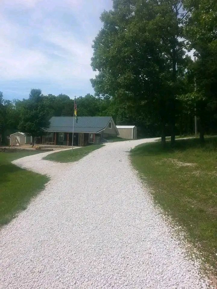 Gravel driveway leading to a small house and trees on a sunny day