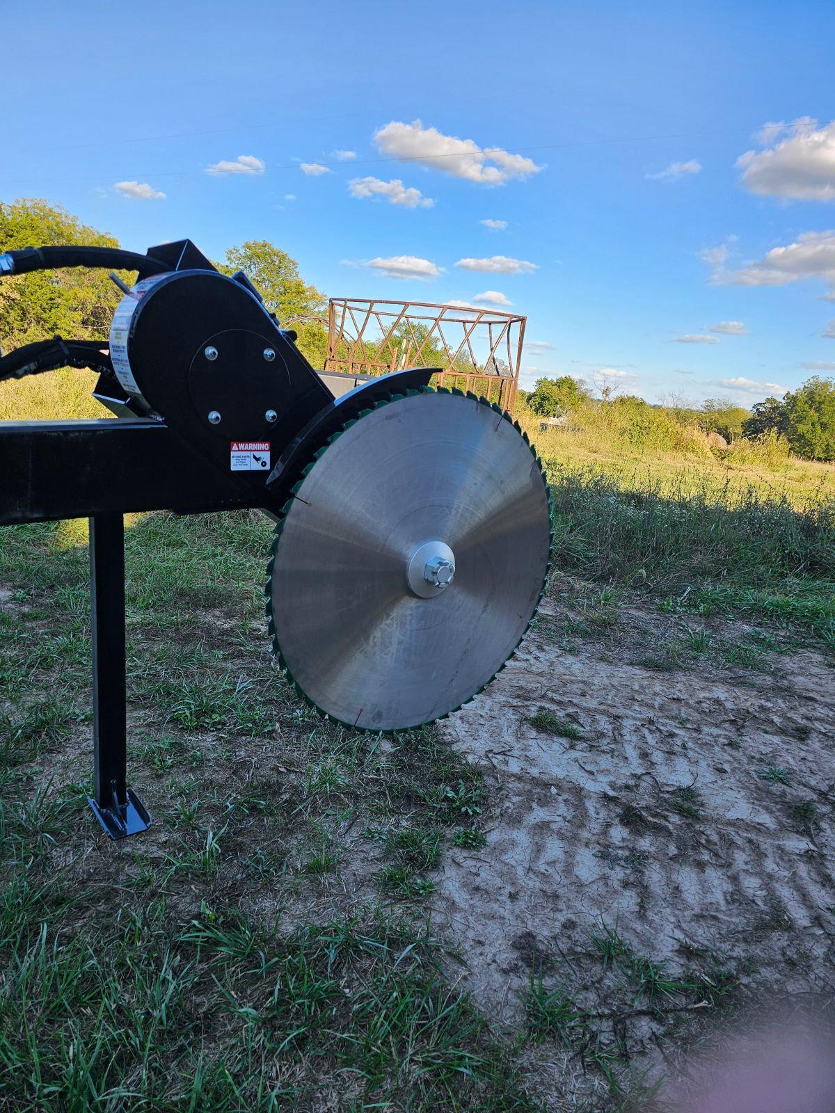 Large metal disc and black machine on a grassy field under a blue sky