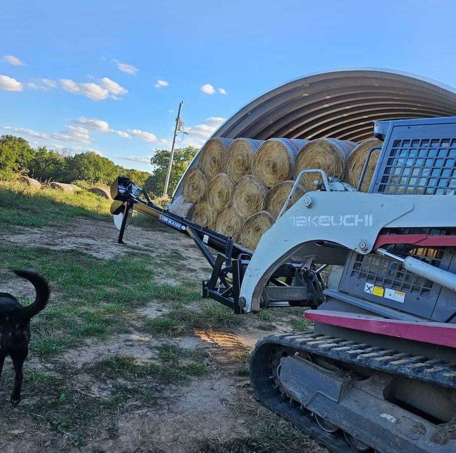 Farm machinery loading round hay bales in a field under a blue sky