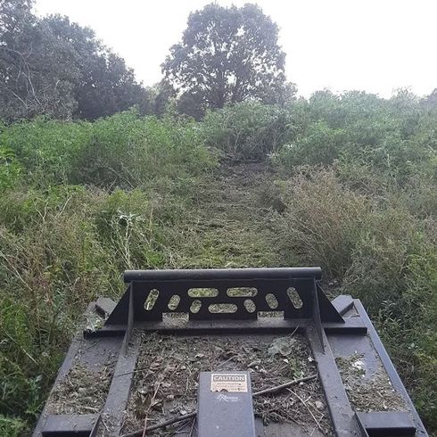Overgrown trail with a metal skid steer attachment in the foreground