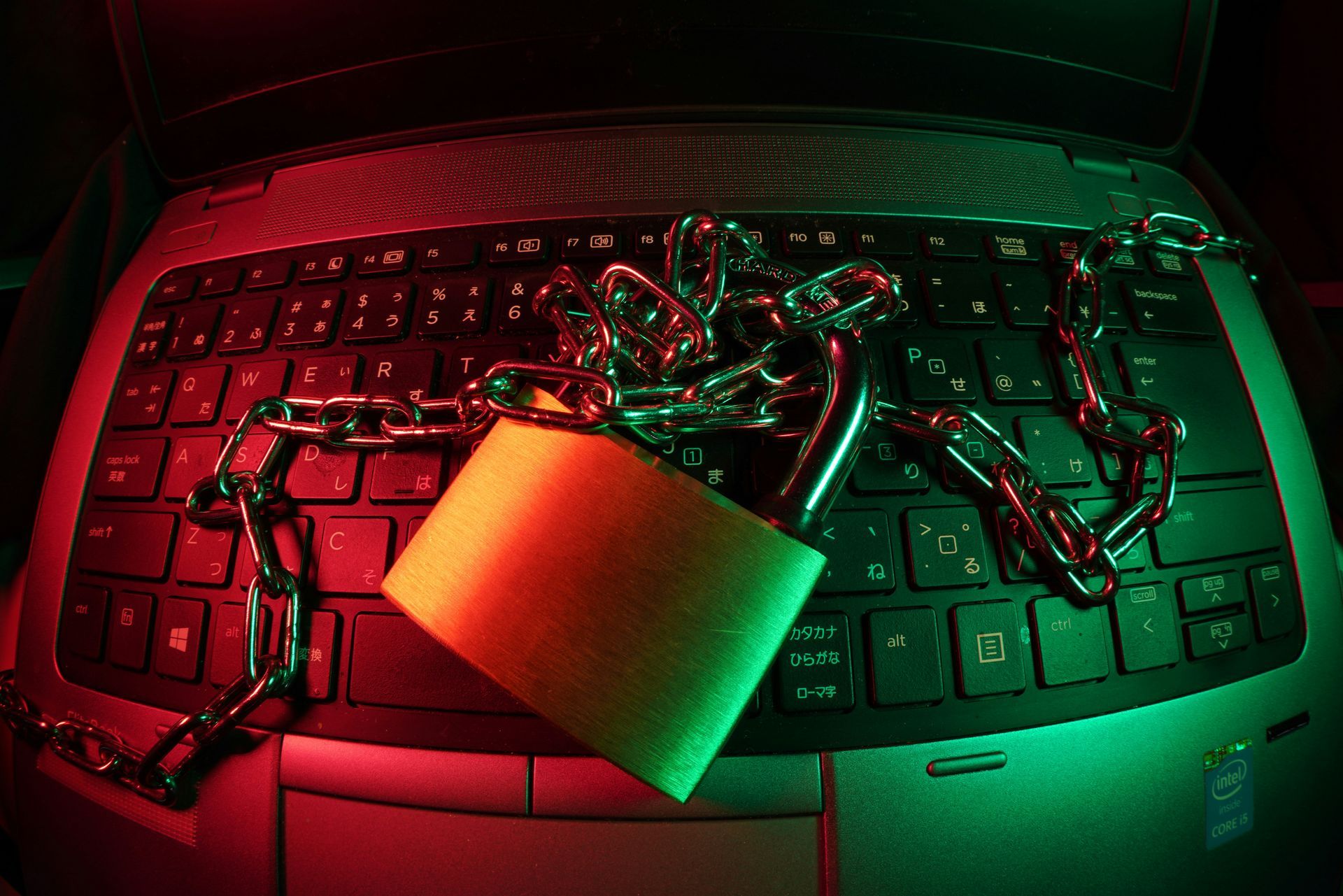 Laptop keyboard secured with a padlock and chain, illuminated with red and green lighting.