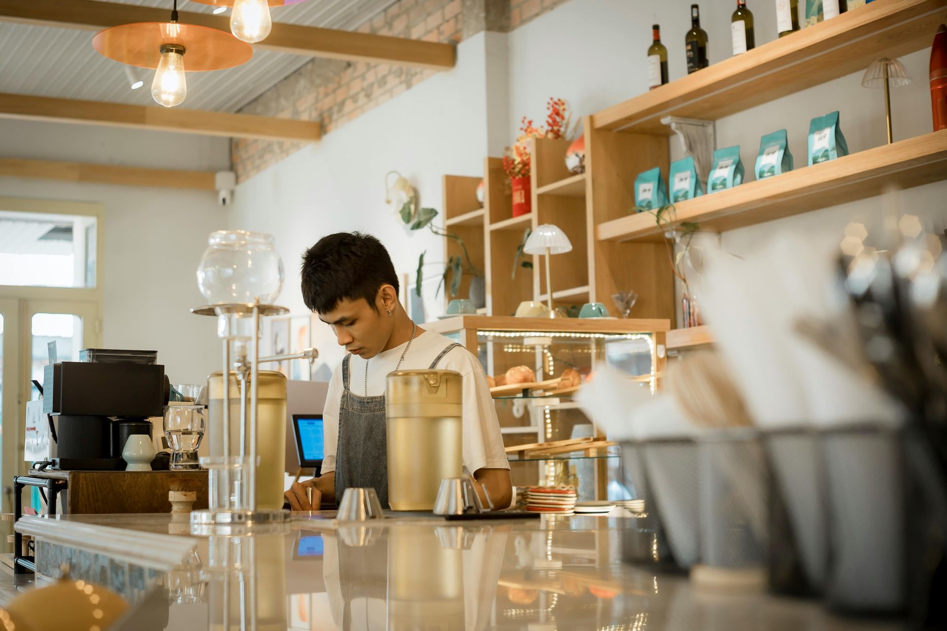 A barista in a cafe, wearing an apron and working behind a counter filled with coffee equipment.