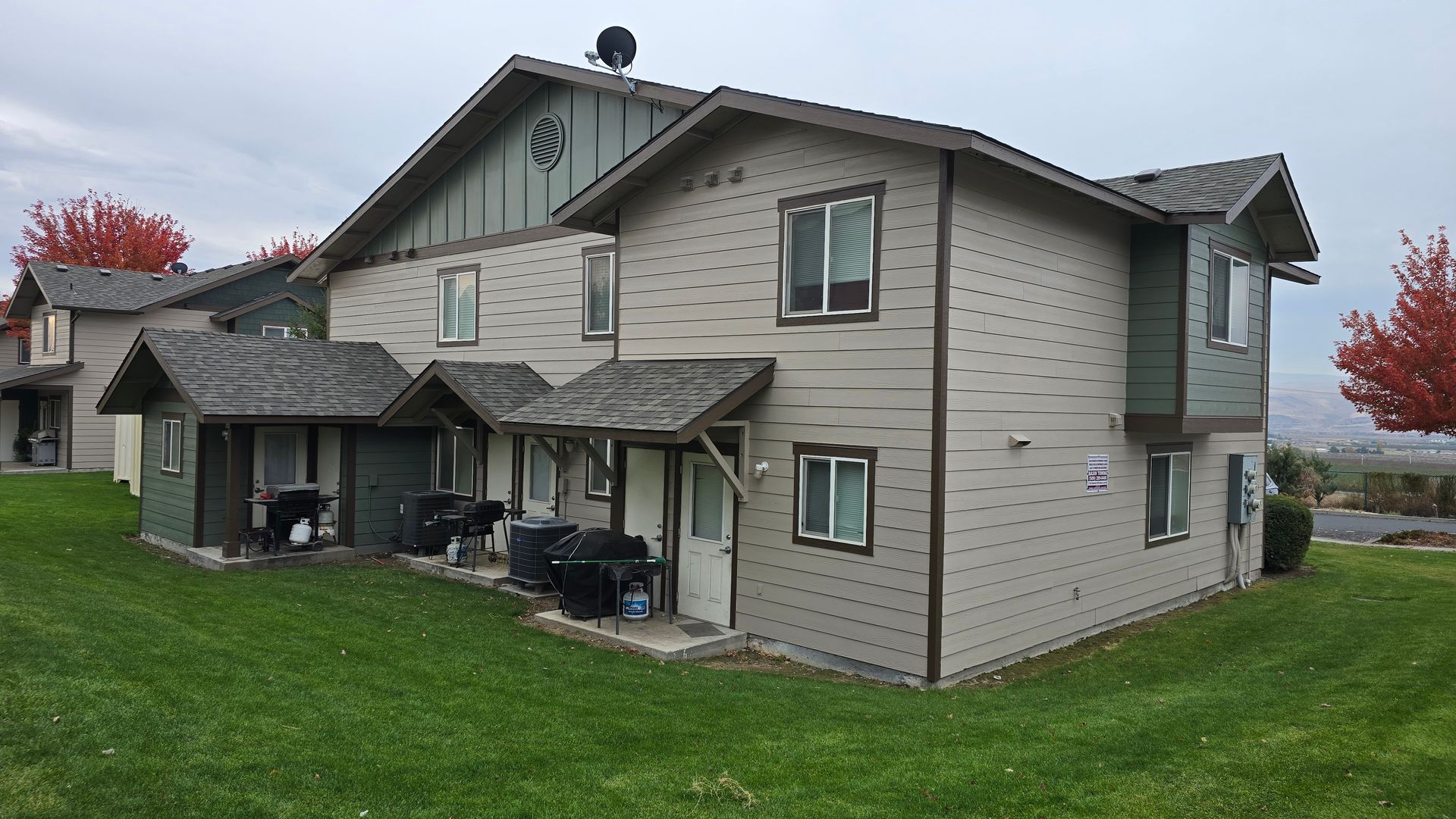 Two-story townhouses with gray siding, green trim, and grass lawns under a cloudy sky.