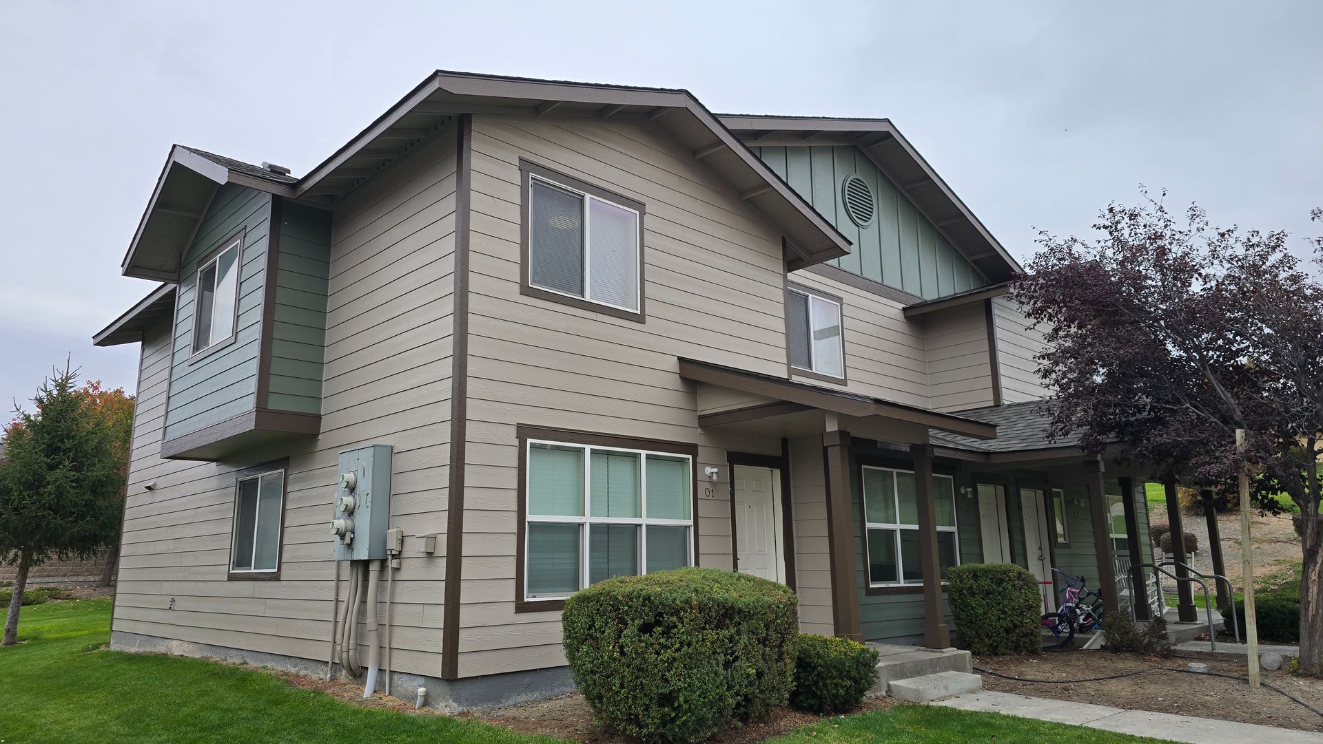 Two-story beige house with brown trim and windows under a cloudy sky.