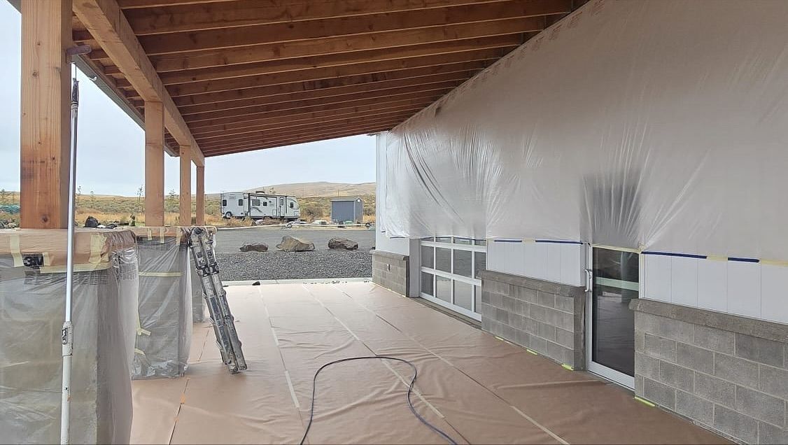 Exterior of a building under construction, with a covered porch and plastic sheeting. Cinderblock walls are visible.