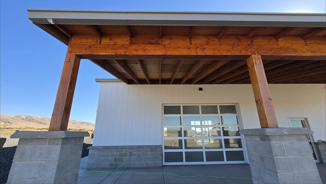 Covered porch with wood beams and pillars, white building, glass garage door, clear sky.