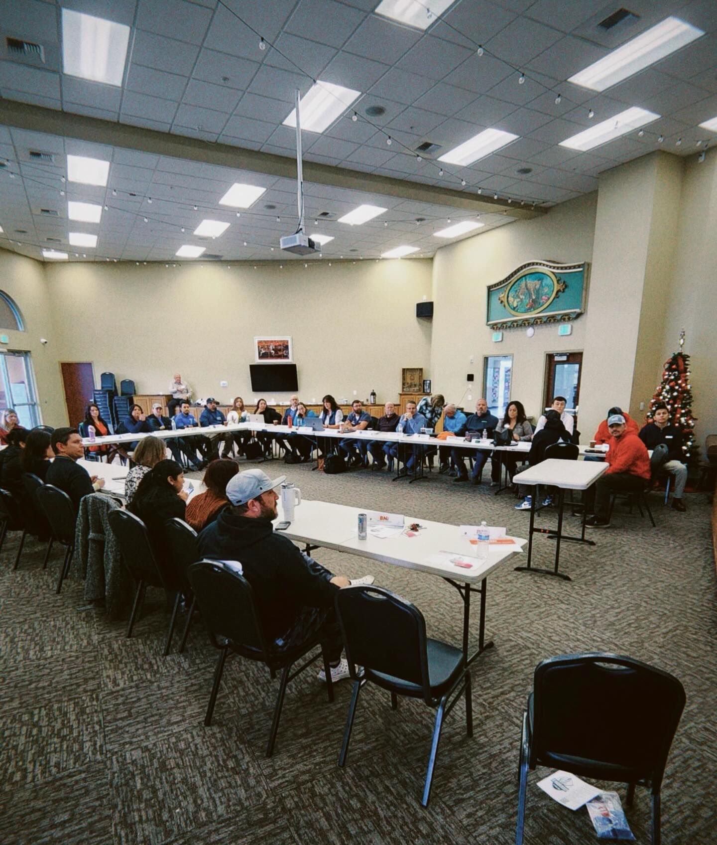 People seated around a long table in a large room. They are engaged in a meeting, some taking notes.