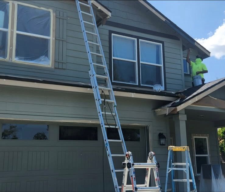 House being painted; painter on a ladder applying new paint to the siding.