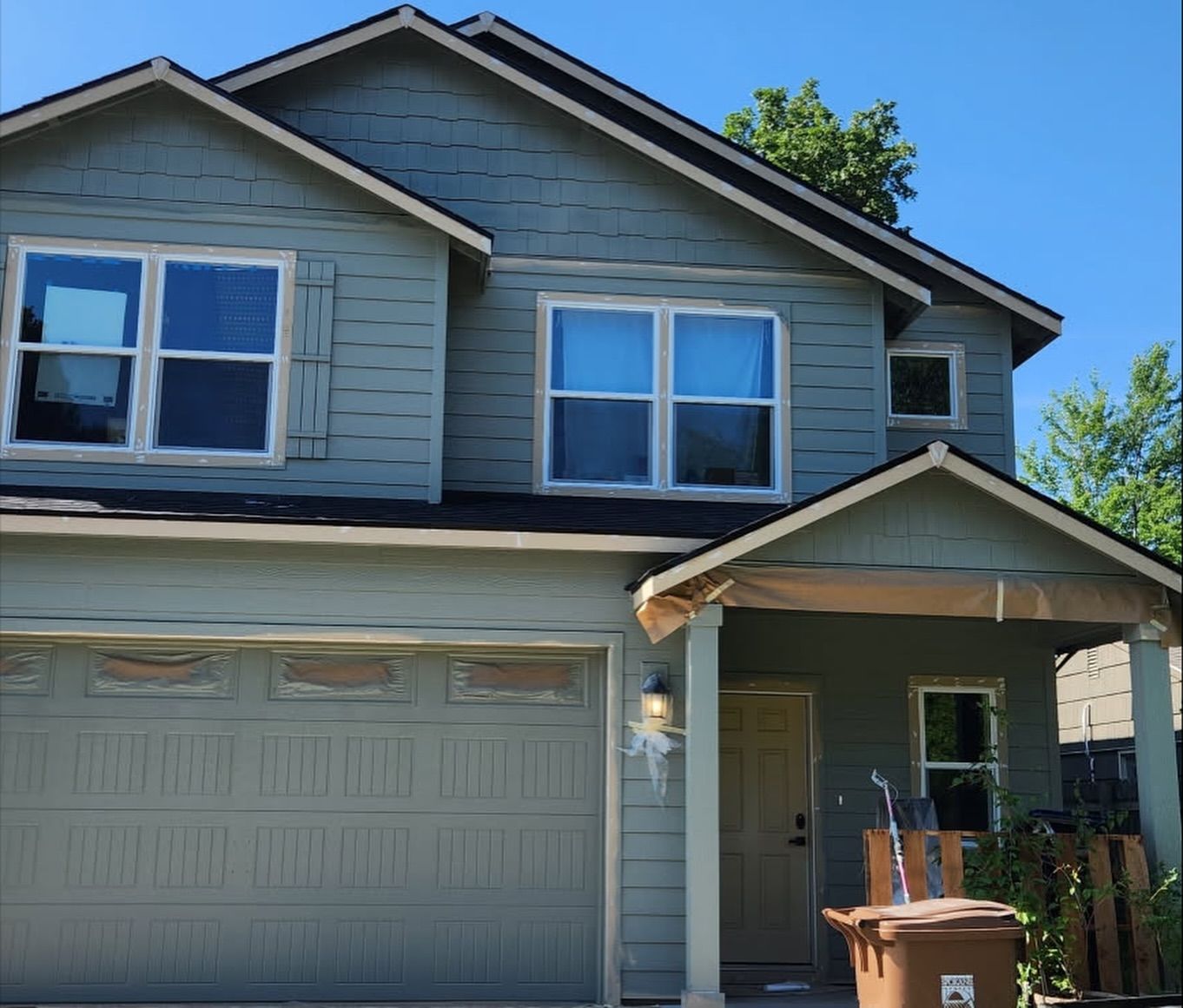 Two-story house with green siding, a garage, and a small porch. Bright blue sky overhead.