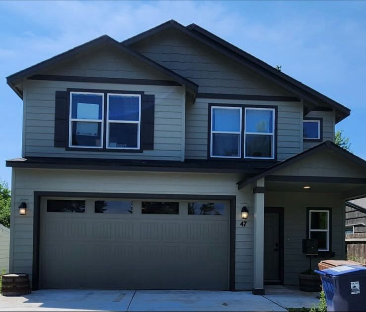 Two-story house with green siding, dark trim, and a two-car garage under a blue sky.