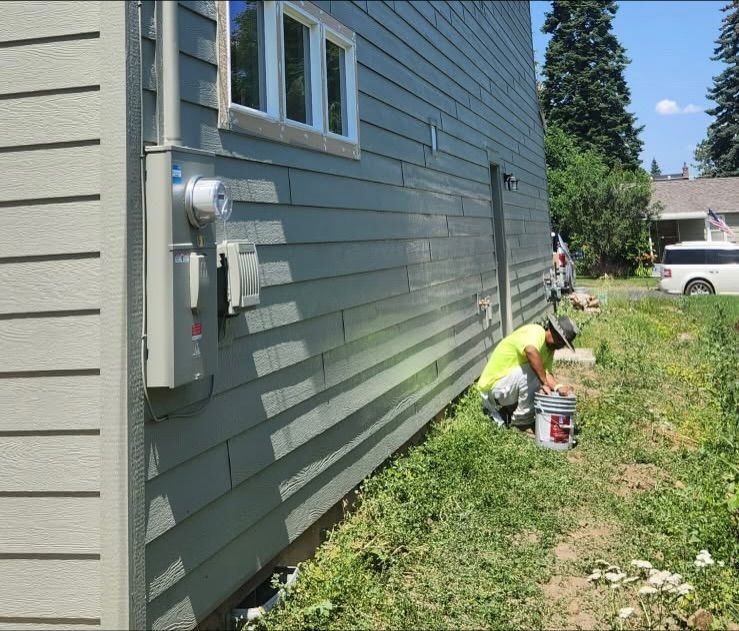 light green siding, white trim, electric box, person wearing yellow shirt kneeling.
