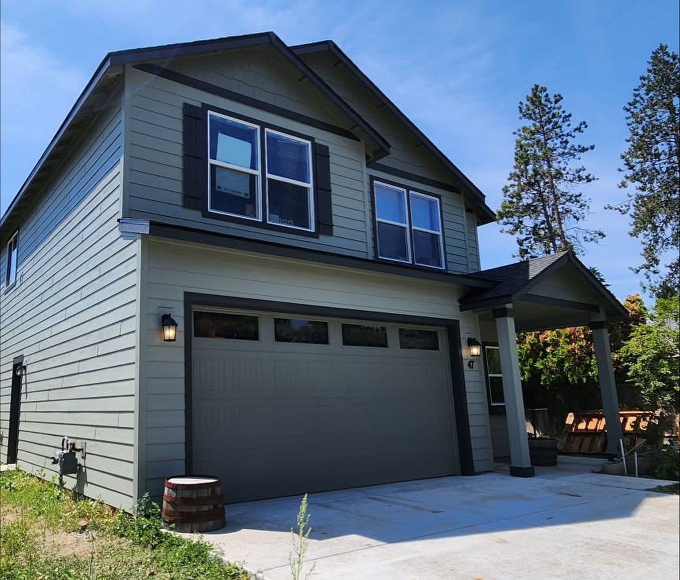 Two-story house with green siding, a garage, and a covered porch. Blue sky.