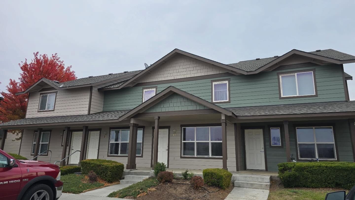 Townhouses with tan and green siding under a cloudy sky, red car in foreground.