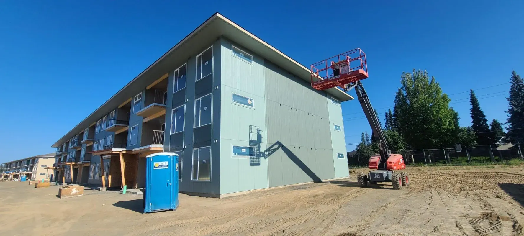 Construction of a multi-story building. A scissor lift is extending to the roof. Blue sky.