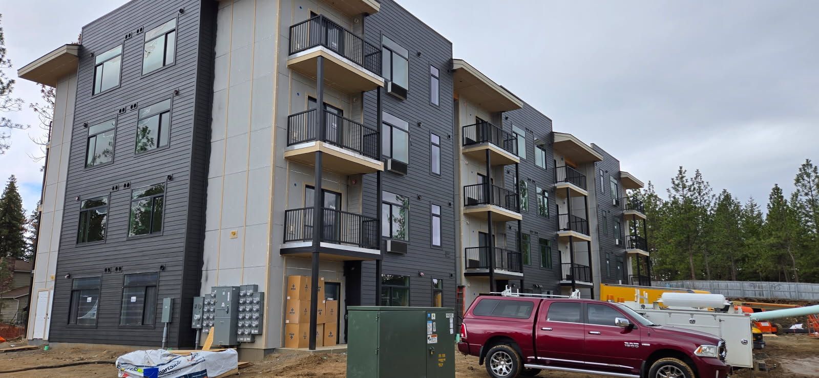 Multi-story building under construction with balconies, dark siding, and a red pickup truck.