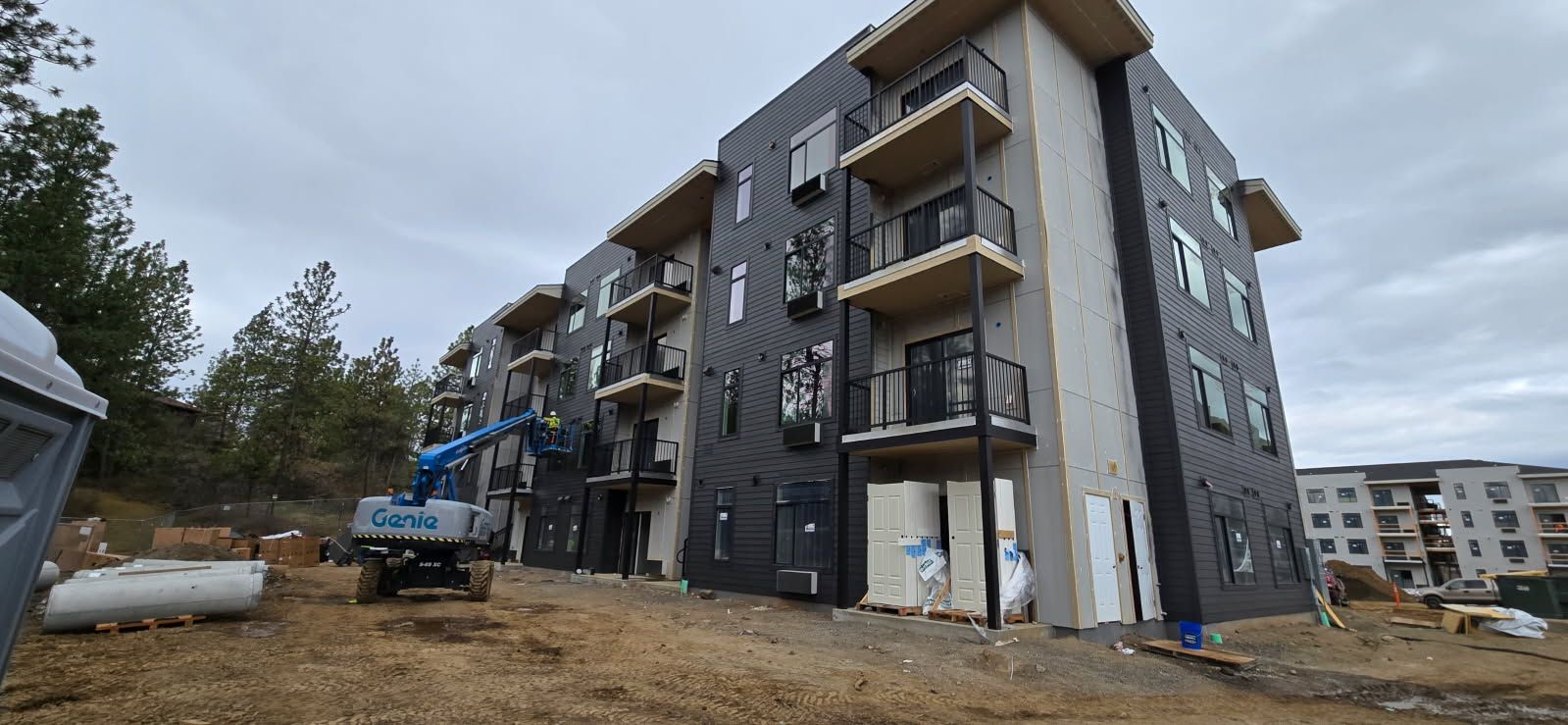 A multi-story building under construction with balconies; a blue lift is present. Overcast sky.