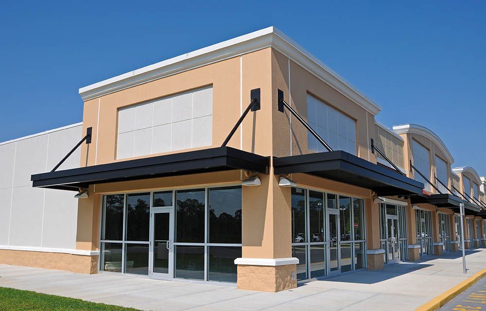 Tan commercial building with black awnings, glass windows, and white trim against a blue sky.