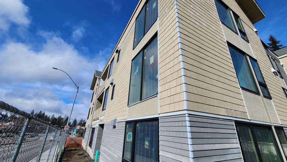 Multi-story beige building with large windows under a partly cloudy blue sky.