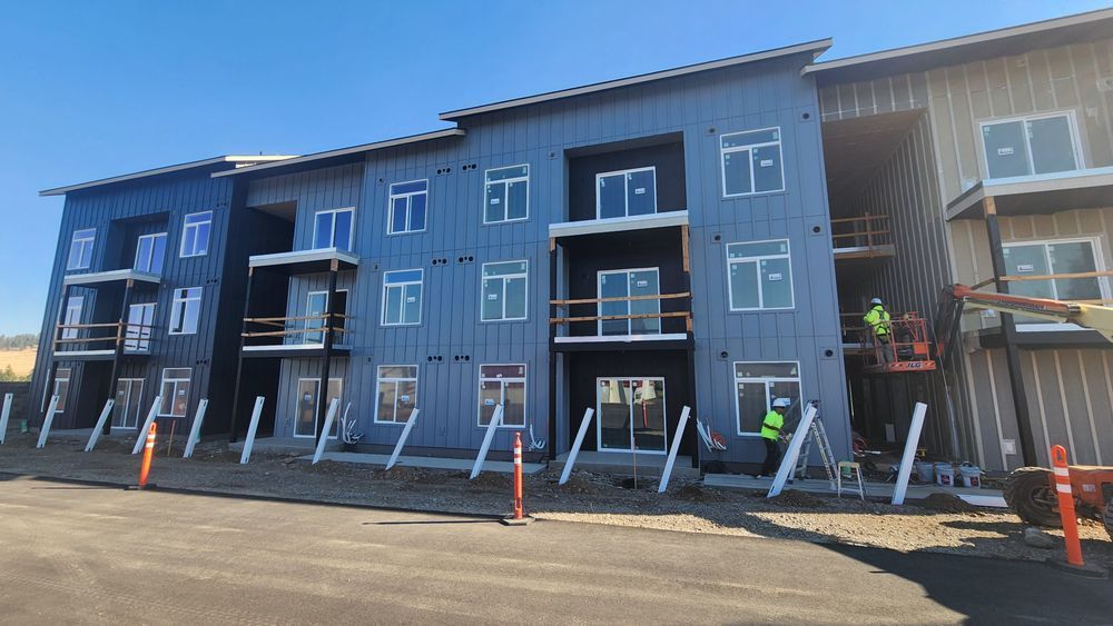 Apartment building under construction; blue siding, balconies, workers on lift.