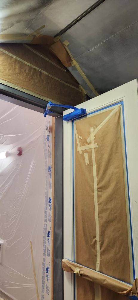 Door frame with blue tape and paper covering, possibly for painting, inside a building.