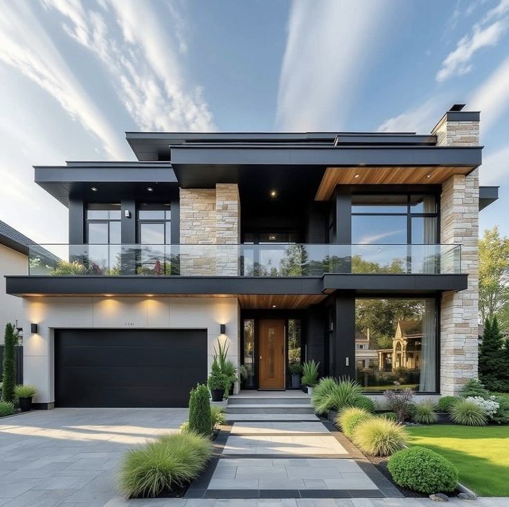 Modern two-story house with stone and black accents, glass balconies, and manicured landscaping.