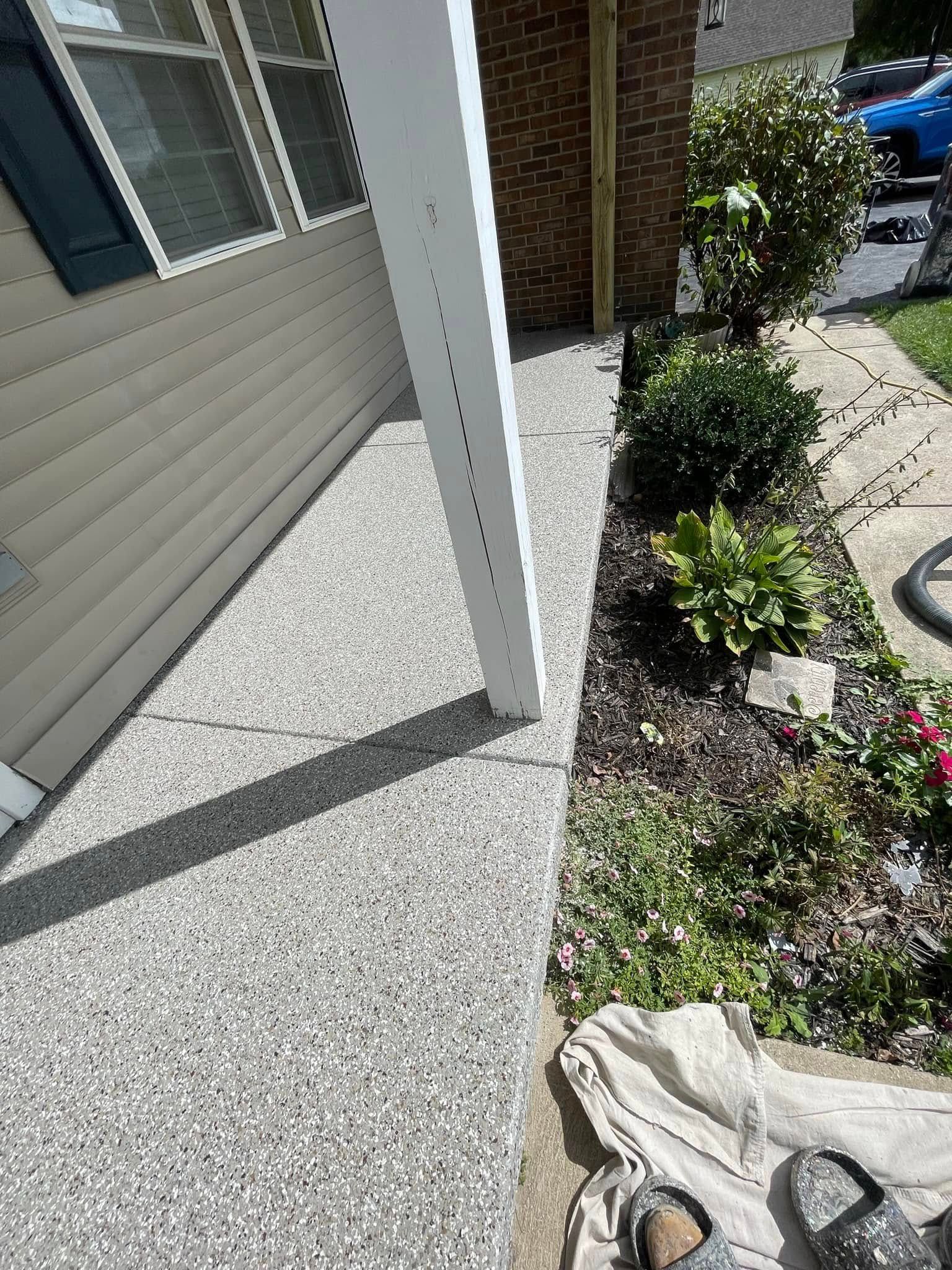 Concrete walkway next to a flowerbed, house and column. Paint rags and work boots visible.