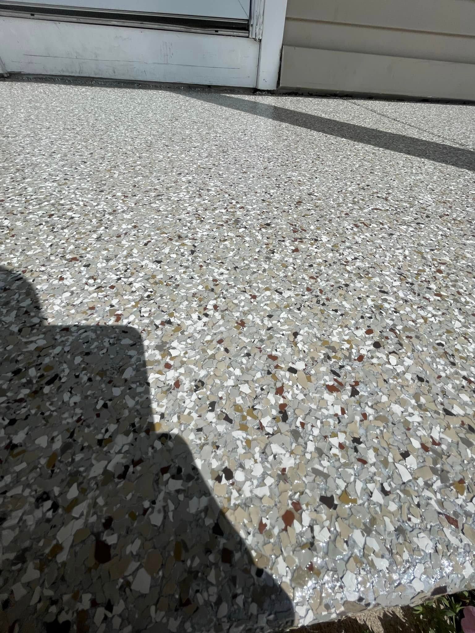 Concrete patio with light and dark chips under a house with white siding.