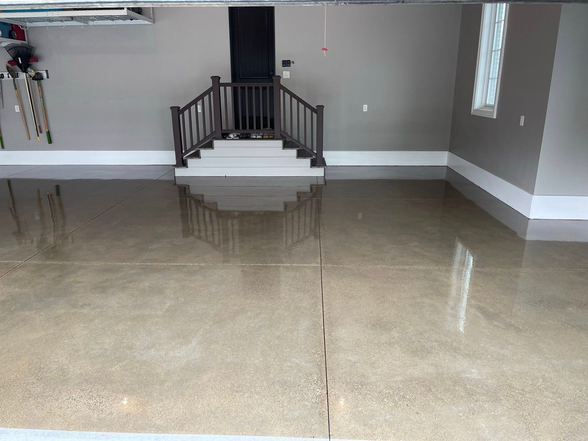 A spacious garage with a shiny, light brown floor. Stairs lead to a dark door, with a white trim.