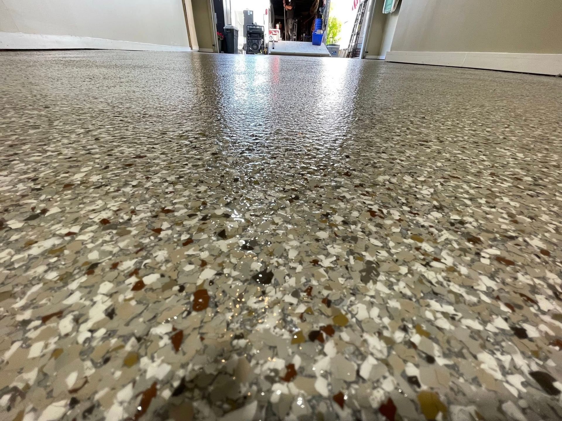 Close-up view of a shiny, speckled epoxy floor in a garage, with the open doorway in the background.