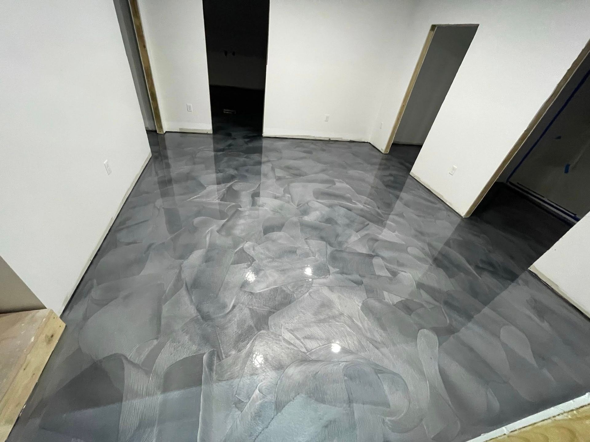 Metallic epoxy floor in a room with white walls, doorways, and unfinished trim.