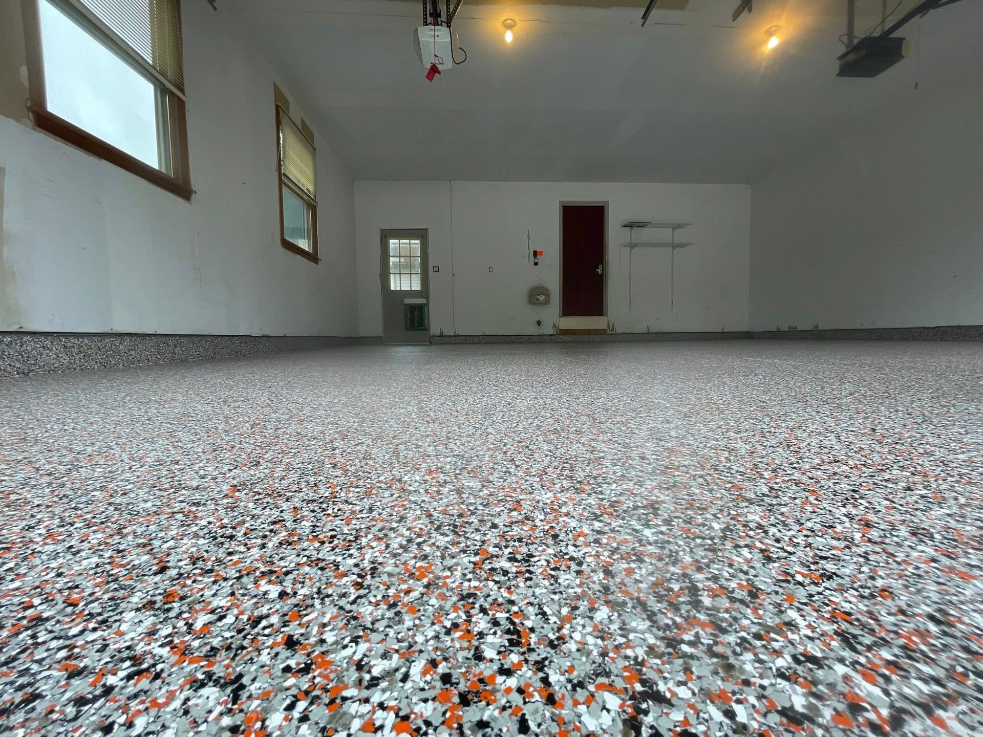 Garage with a speckled gray, white, and orange epoxy floor; white walls; red door.